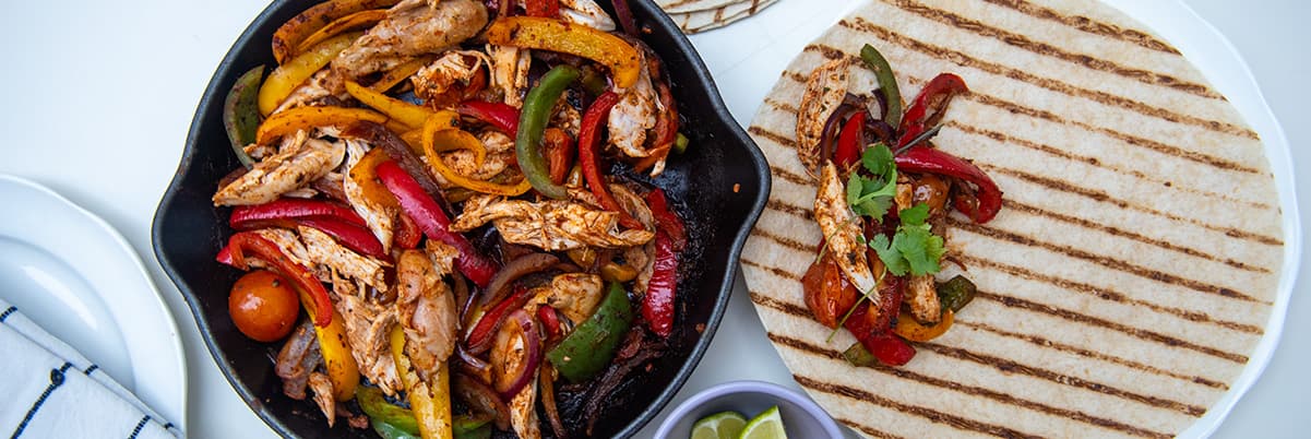 A tortilla with some filling on a plate next to a pan full of filling